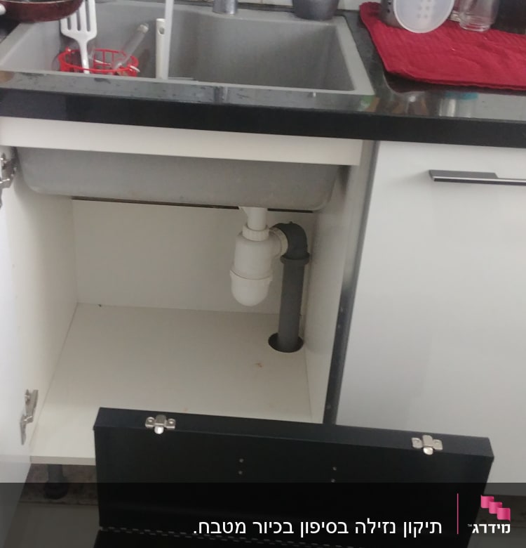 ארגז כלים פתוח ליד כיור מטבח עם צנרת גלויה